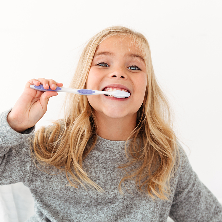 Close-up portrait of cute kid in gray pajamas brushing her teeth, looking at camera